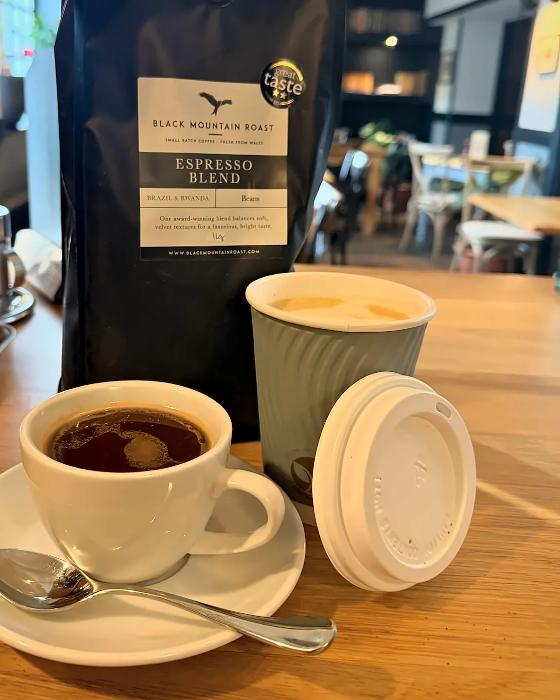 An americano in a white cup beside a takeaway cup and a bag of Black Mountain Roast espresso blend.